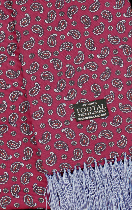 A close-up of a patterned scarf with a magenta background, featuring a repeating paisley and floral motif in white, brown, and gray, finished with a light blue fringed edge. A black woven label reads 'AUTHENTIC TOOTAL TEEDILIZED'.